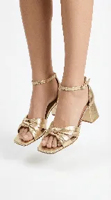 Sandalia de tacón medio ancho con diseño de nudo frontal y pulsera ajustable al tobillo con hebilla metálica.