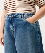 Pantalón de jean azul con lavado medio, corte barrel de piernas amplias, cintura con pasacintos, bolsillos funcionales y pinzas en las piernas.