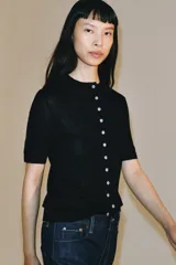 Chaqueta de punto fino color negro, con cuello redondo, manga corta y cierre frontal con múltiples botones a contratono.