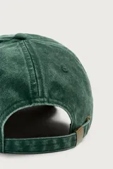 Gorra de siete paneles verde oscuro con efecto lavado, visera curva y bordado frontal en tono amarillo con la inscripción 'Bahia Montego'. Cuenta con ajuste posterior.