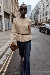 Chaqueta de cuello redondo y manga larga con diseño peplum en el bajo. Confeccionada en tejido efecto ante, cuenta con cierre frontal de cremallera y cinturón fino ajustable en la cintura.