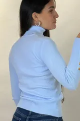 Polera de hilo blanca de cuello alto y manga larga, con detalle de botones dorados en los puños. Tejido de punto acanalado ajustado al cuerpo.