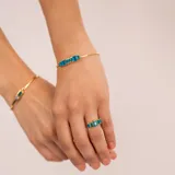 Anillo dorado con cinco piedras rectangulares de color azul.