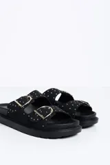 Sandalia plana color negro con dos tiras ajustables mediante hebillas metálicas doradas, decoradas con pequeñas tachas doradas. Cuenta con una suela anatómica y plantilla cómoda.