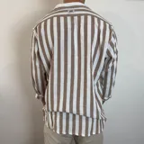 Camisa de lino de corte oversize con diseño de rayas verticales en tonos blanco y tostado, manga larga y cierre frontal con botones.