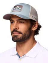 Gorra tipo trucker Columbia de color celeste con malla trasera en tono beige. Cuenta con un parche frontal bordado con diseño de montañas y el logo de la marca.