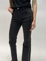 Jean de denim negro tiro alto con detalles de tachas metálicas en los laterales de las piernas.