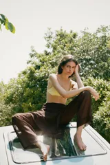 Falda pantalón de tiro alto en color marrón oscuro, con diseño superpuesto que combina una falda envolvente con lazadas laterales y un pantalón de corte recto debajo. Cuenta con cierre lateral oculto.