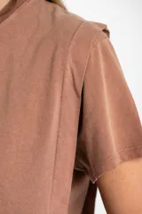 Remera de algodón color mostaza/naranja quemado, con cuello redondo y mangas cortas. Presenta un diseño con costuras externas visibles en los hombros y laterales, dándole un aspecto desestructurado.