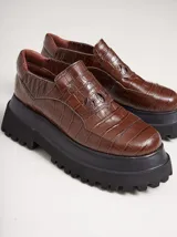 Mocasines de plataforma alta con diseño de estilo rebelde. Presentan un estampado de cuadros en tonos violeta y amarillo, confeccionados en lona con detalles en cuero. Cuentan con una suela robusta y elásticos laterales ocultos para facilitar el calce.