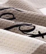 Remera tipo polo de corte oversized, confeccionada en tejido de punto con diseño de rayas verticales en tonos beige y blanco. Presenta cuello clásico, abertura frontal con botones y bordado con la inscripción 'The Hamptons New York' en el pecho.