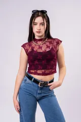 Polera cropped de encaje color bordó con diseño floral, cuello alto y mangas casquillo. Presenta una textura semitransparente y un ajuste entallado.