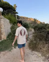 Remera oversize color beige de corte holgado, con estampa en la espalda que representa un esqueleto dentro de un ataúd con rayos oscuros y texto descriptivo.