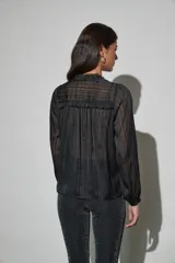 Blusa negra de tela semitransparente con diseño de rayas verticales texturizadas, cuello con volados y cierre frontal de botones.