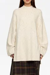 Sweater de punto color crema con neps negros, de corte recto y holgado, con cuello alto tipo mock neck y mangas largas con puños acanalados.