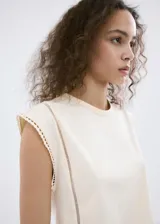 Camiseta sin mangas color beige, con cuello redondo y detalles de encaje en las costuras de los hombros y laterales.