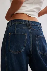 Jean de denim azul con silueta barrel y tiro medio, piernas amplias que se afinan en los tobillos, desgastes sutiles y costuras en las piernas.