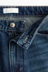 Jean de tiro alto y diseño barrel en denim de algodón azul, con corte de cinco bolsillos, cierre frontal con botón y cremallera, y piernas de corte curvo y holgado.