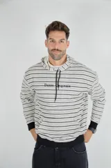 Hoodie de corte holgado con estampado de rayas horizontales en blanco y negro. Presenta capucha con cordones ajustables, bolsillo tipo canguro frontal, puños y ruedo en color negro sólido, y el logo de la marca bordado en el pecho.