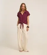 Blusa de manga corta con cuello camisero, abotonadura frontal y detalle de lazo anudado en el bajo. Confeccionada en tejido texturizado con caída fluida.