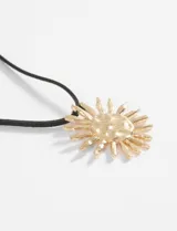 Collar de cordón negro con dije metálico plateado en forma de sol con textura central.