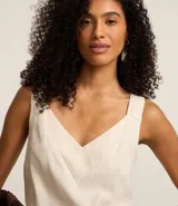 Blusa sin mangas color beige claro, confeccionada en tejido plano de viscolino. Presenta un escote en V cruzado y breteles anchos con detalle texturizado.