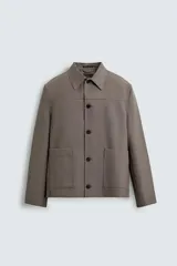 Sobrecamisa de corte relajado confeccionada en tejido compacto con lana. Presenta cuello solapa, cierre frontal con botones, mangas largas con puños abotonados y dos bolsillos de plastrón en la parte frontal.