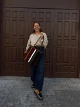 Cartera tipo tote de cuero con diseño de franjas verticales multicolores en tonos tierra, rojo y azul. Cuenta con correas trenzadas de cuero y cierre superior.