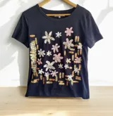 Remera de manga corta color negro, con cuello redondo y diseño pintado a mano de flores en tonos nude y cobre, de la marca Carolina de Cunto.