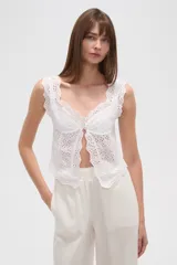 Top blanco de algodón con bordado broderie, corte ajustado al cuerpo, breteles finos y escote redondo. Presenta un cierre frontal con botones y elástico en la base.