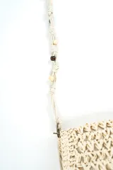 Bandolera beige de tejido rústico estilo crochet con solapa, correa larga con cuentas de madera decorativas y cierre superior.