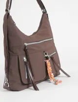 Bolso tipo hobo convertible a mochila, color marrón, con múltiples bolsillos frontales con cierre y herrajes plateados. Incluye un llavero decorativo removible con cuentas de colores y correa regulable.