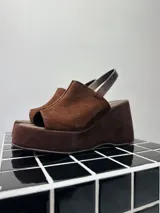 Sandalias de plataforma y taco ancho tipo wedge, confeccionadas en cuero gamuzado color marrón chocolate. Presentan diseño destalonado con tira trasera y capellada cerrada con apertura en la puntera (peep toe).