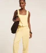 Pantalón zanahoria de tiro alto color amarillo pálido, confeccionado en viscolino con 15% de lino, con trabillas en la cintura, solapas con botón abajo de la cintura, pliegues y cierre tradicional.