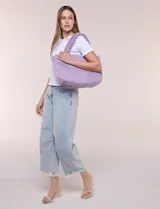 Cartera tipo shopper color lila con textura efecto peluche, de estructura flexible y amplia apertura con botón metálico. Cuenta con doble asa superior fija texturada.