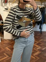 Sweater a rayas horizontales en tonos gris y blanco, con apliques de cuero en forma de rombos en el frente. Los rombos están confeccionados con piezas de cuero en colores negro, marrón y verde musgo, unidas con costuras a la vista.