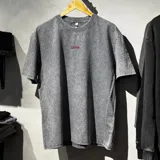 Remera oversize de algodón con efecto stone wash en color gris, manga corta y cuello redondo. Presenta un pequeño bordado en hilo rojo en la parte posterior con la palabra "Become.".