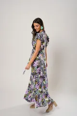 Vestido largo con estampado floral en tonos lila, verde y negro. Tiene escote en V, mangas cortas con volados y corte cruzado con lazo en la cintura.