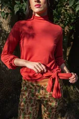 Remera color ladrillo de viscosa, con cuello alto, mangas largas abullonadas y lazo lateral en la cintura.