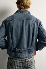 Campera de denim de algodón en color azul, con lavado efecto desgastado, cuello solapa y cierre frontal de botonadura metálica. Presenta bolsillos con solapa en el pecho, mangas largas con puños abotonados y trabilla ajustable en la cintura posterior.