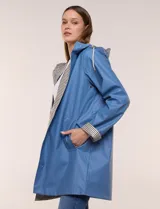 Pilot engomado impermeable color azul, de corte recto estilo trench con acabado resistente al agua. Cuenta con capucha integrada, cierre frontal con broches a presión, bolsillos laterales con ojal y forro interior de tela estampada a cuadros visible en la solapa y los puños.