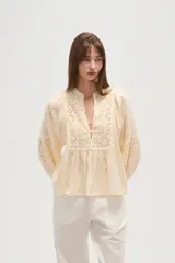 Blusa de viscosa color blanco con diseño holgado, cuello en V y cierre frontal con botones. Presenta detalles de bordado tipo broderie en el frente y en las mangas abullonadas.