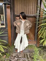 Campera de jean marrón suave con apliques de flores de crochet en el pecho, costuras decorativas artesanales en cuello y bordes, bolsillos frontales y cierre con botones.