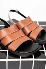 Sandalias chatas color marrón con tiras anchas de cuero y pulsera al tobillo con hebilla metálica.