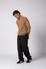 Sweater de tejido de punto grueso color tostado, con cuello redondo y mangas largas con puño elástico que incluye una etiqueta decorativa.