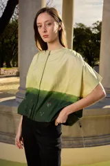 Camisa de algodón de manga corta, con diseño degradado en tonos amarillo y verde, y detalles bordados de flores en la parte inferior. Cuenta con cierre frontal de botones ocultos y cuello redondo.