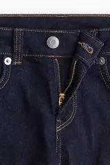 Jeans de denim color azul oscuro, tiro bajo, corte ajustado en muslos y acampanado desde la rodilla. Presenta cierre y botón frontal, bolsillos abiertos delanteros y bolsillos traseros con solapa y botón.