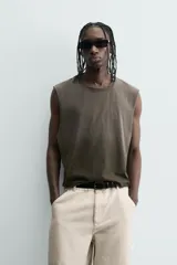 Camiseta tipo tank (sin mangas) de corte cropped fit, color gris oscuro con efecto gastado. Presenta cuello redondo y un pequeño parche rectangular con texto en la parte inferior delantera.