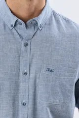 Camisa de lino de manga corta con sutil patrón de cuadros pequeños, cuello camisero abotonado, bolsillo en el pecho con logo bordado y cierre frontal de botones.