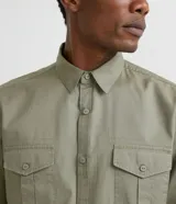 Camisa verde militar de manga larga en sarga de algodón, con cuello clásico, cierre frontal abotonado y dos bolsillos con solapa abotonada en el pecho.